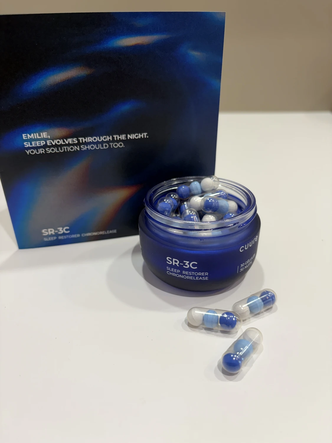 J'ai testé SR-3C de Cuure pour mon sommeil : mon avis complet 2 Flacon en verre bleu du complément sommeil Cuure SR-3C ouvert, avec trois gélules posées devant et la carte personnalisée